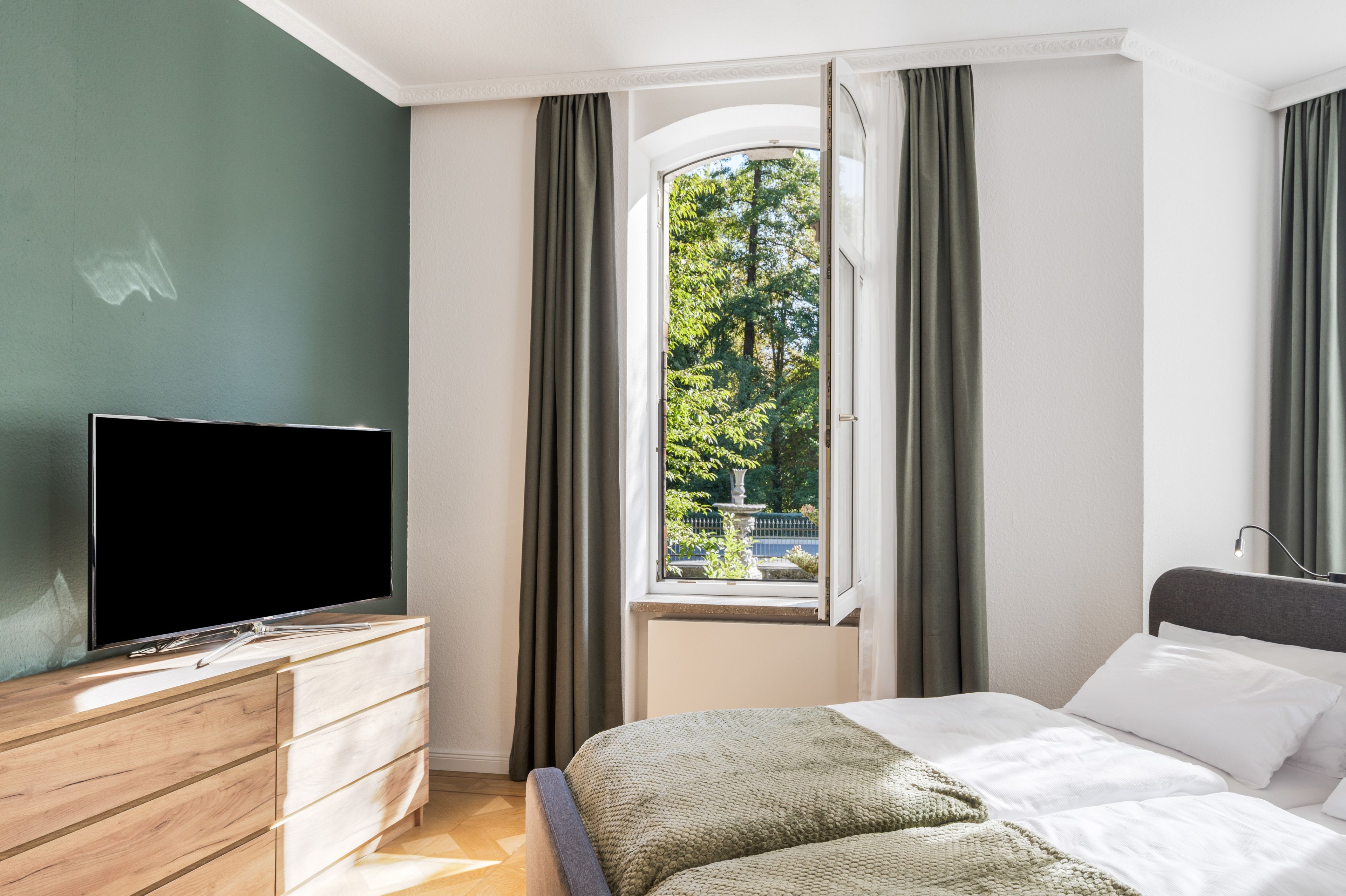 Une chambre d’hôtel avec un lit, un téléviseur posé sur une commode en bois et une fenêtre avec des rideaux.