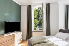 A hotel room with a bed, a TV on a wooden dresser, and a window with curtains.