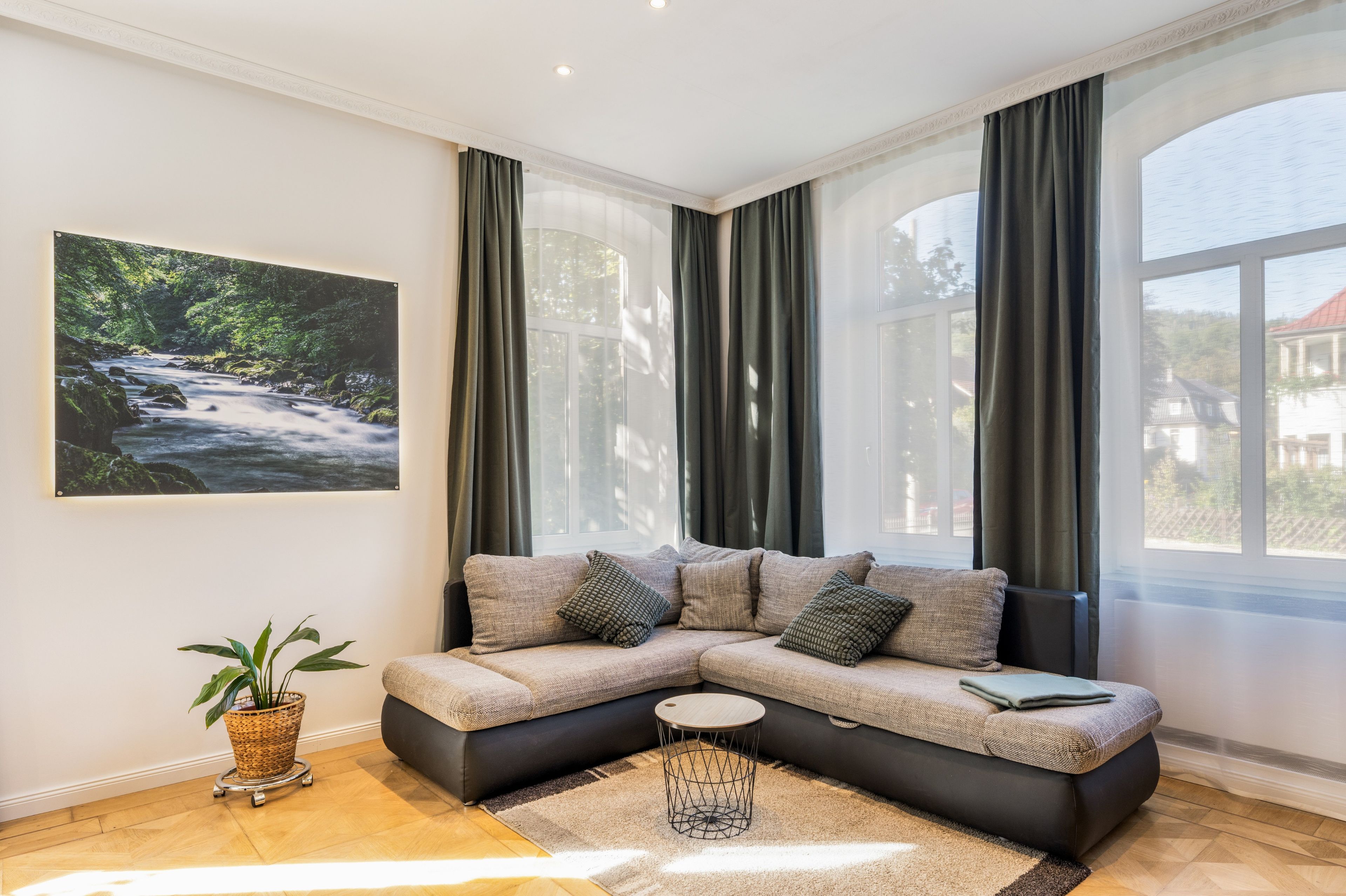 Ein modernes Wohnzimmer mit einer Eckcouch, einem kleinen runden Tisch und einem großen Fenster mit Vorhängen.