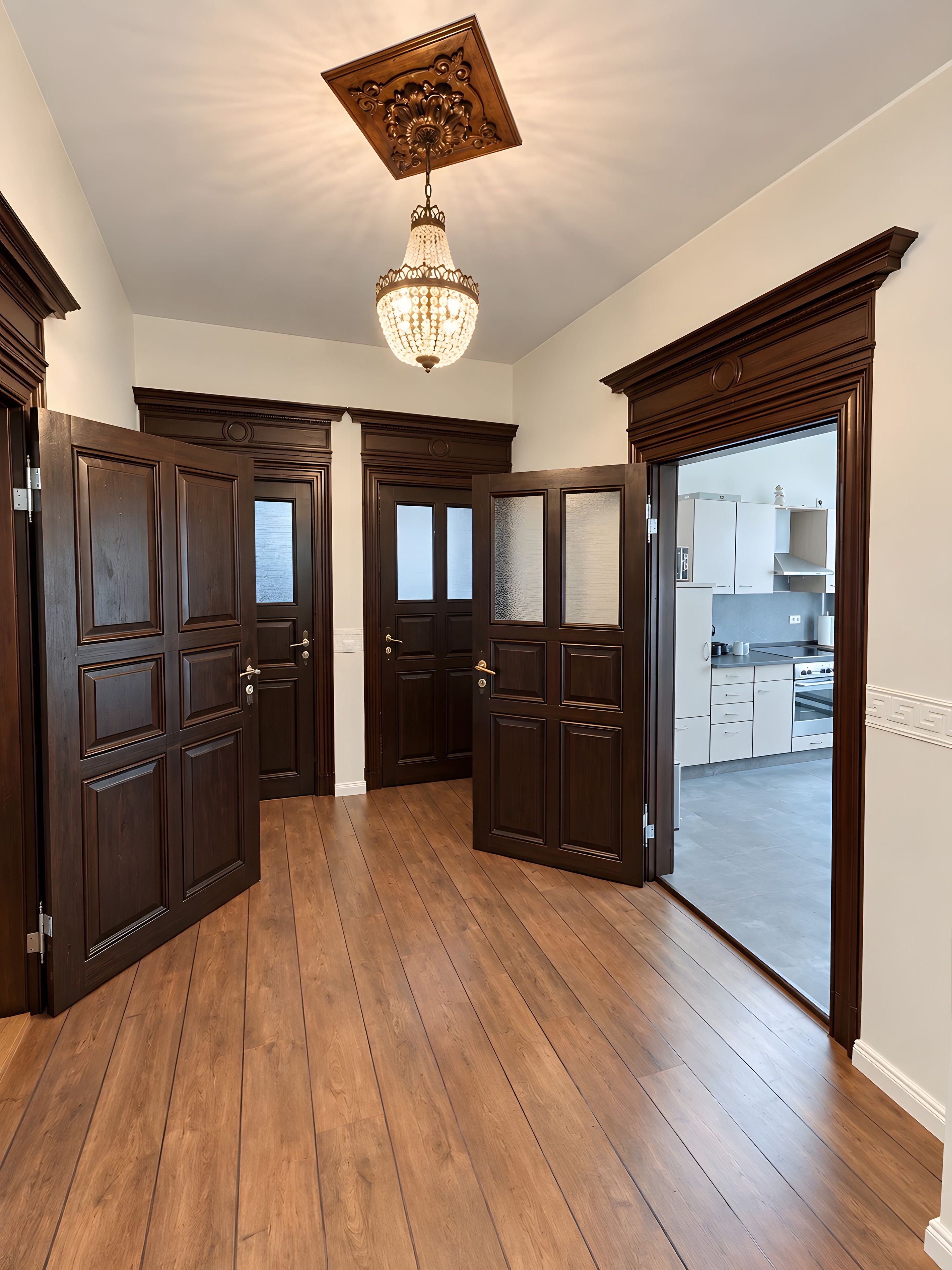 A hallway with dark wooden doors, a chandelier, and a view into a kitchen area.
