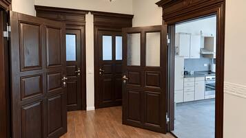 A hallway with dark wooden doors, a chandelier, and a view into a kitchen area.
