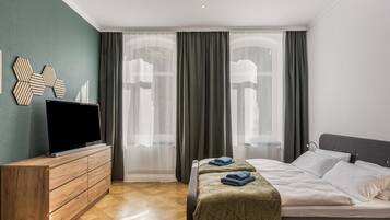 Una habitación de hotel con cama, televisor sobre un aparador de madera y ventana con cortinas.
