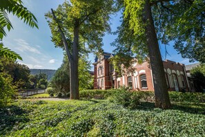 A historic building with a brick facade and arched windows, surrounded by lush greenery and trees.