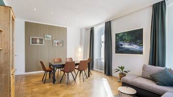 A modern living room with a dining area, a sofa, a coffee table, and a large window with curtains.