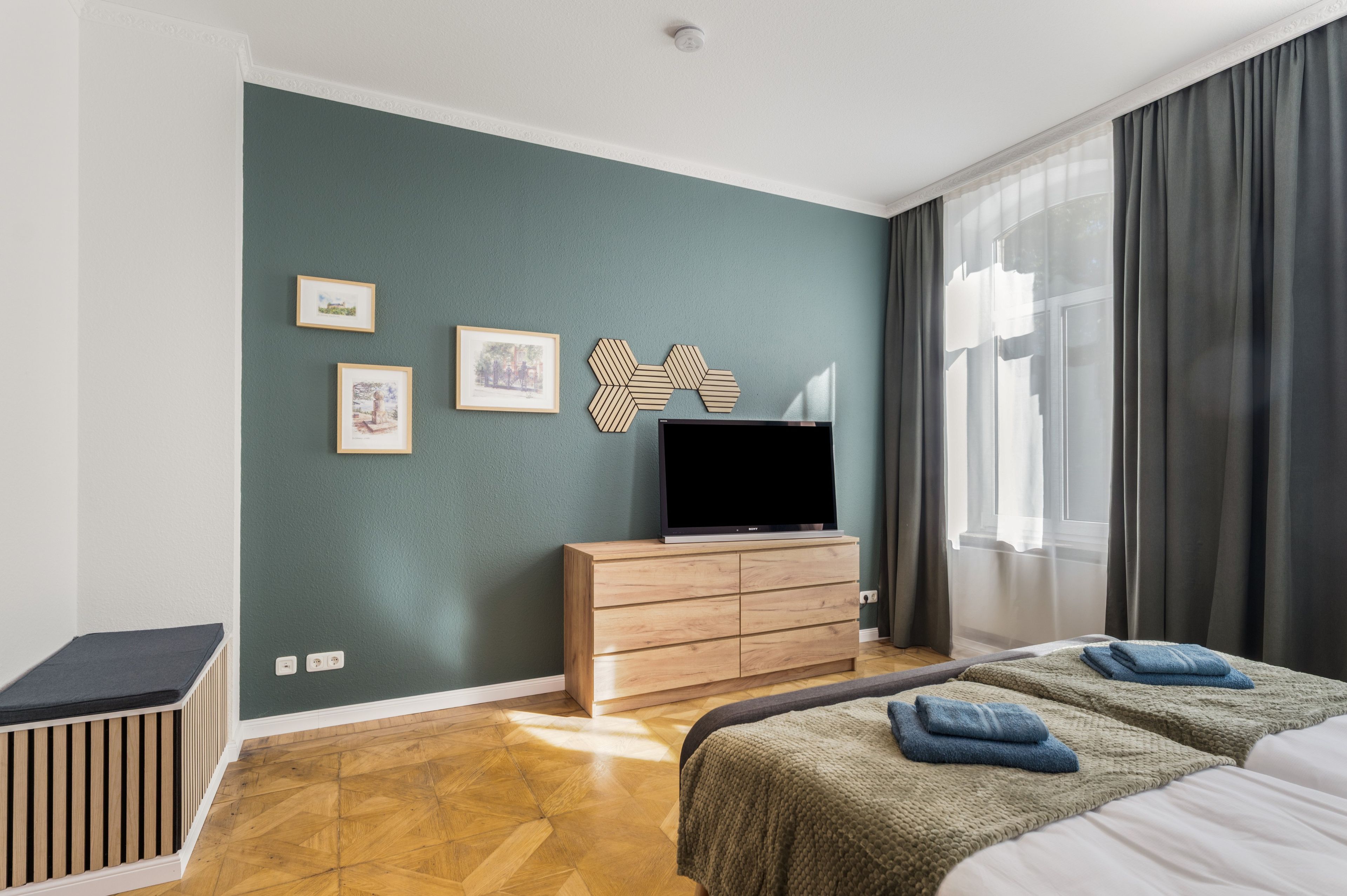 A modern hotel room with a wooden dresser, a flat-screen TV, and a bed with two pillows.