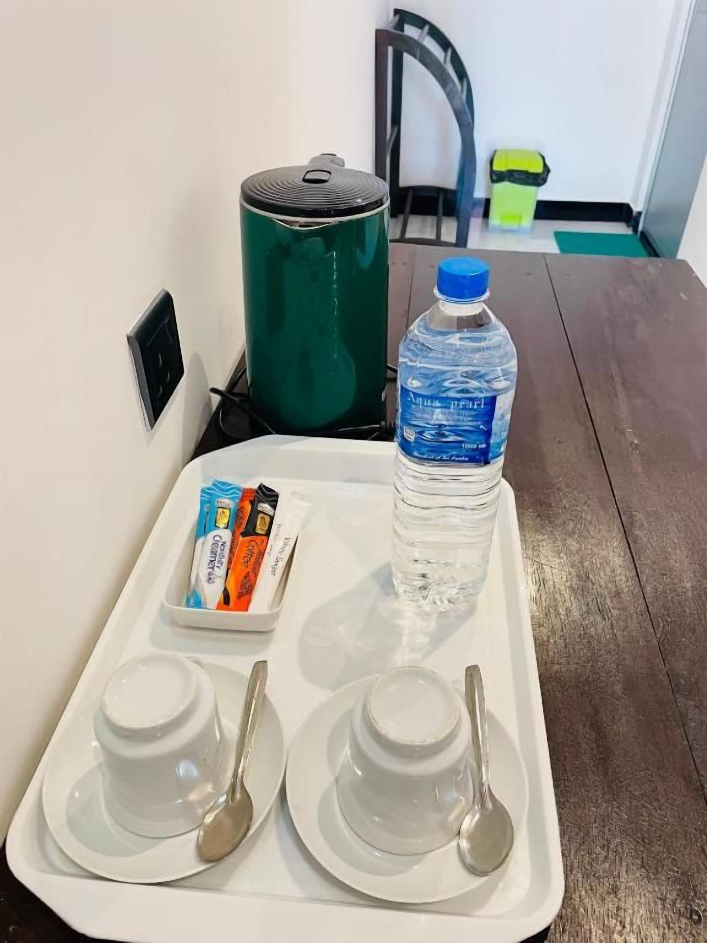 Una bandeja con dos tazones blancos, dos cucharas, una botella de agua y un recipiente pequeño con alimentos.