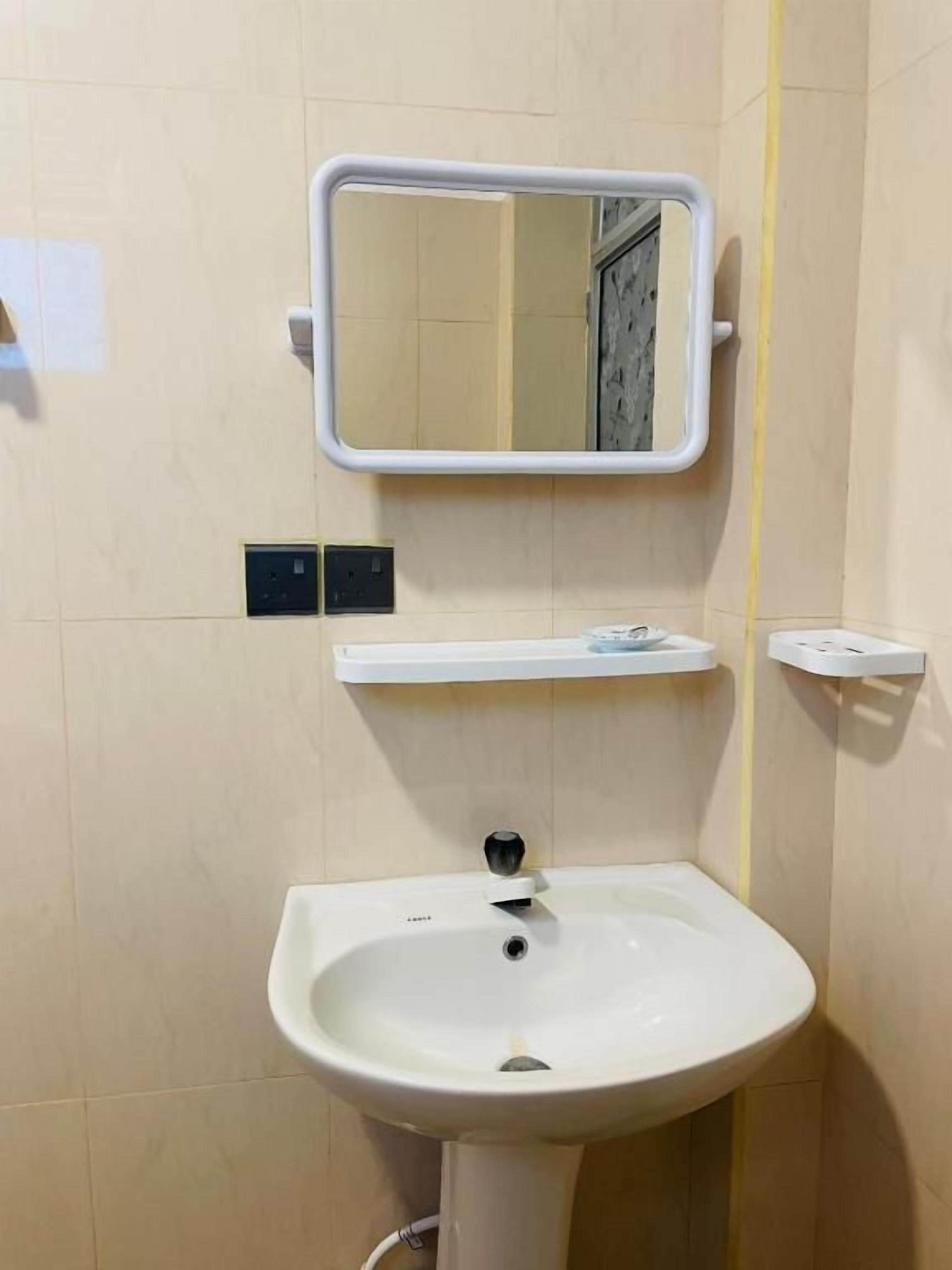 A bathroom with a white sink, a mirror, and a shelf above the sink.