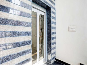 A hallway with a glass door, a tiled wall, and a light switch. - Super Townhouse Pahadiya (Varanasi)