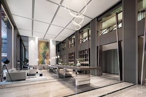 A spacious lobby with a long reception desk, seating area, and a large abstract painting on the wall.