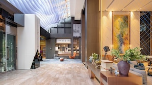A spacious lobby with a high ceiling, a reception desk, seating area, and a large abstract painting. - Atour Hotel Dalian Xinghai Square (Dalian)
