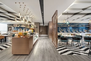 En moderne hotellobby med et centralt barområde, siddepladser og et mønstret gulv.