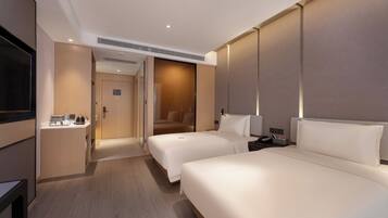 A hotel room with two beds, a TV, a minibar, and a bathroom visible through an open door.