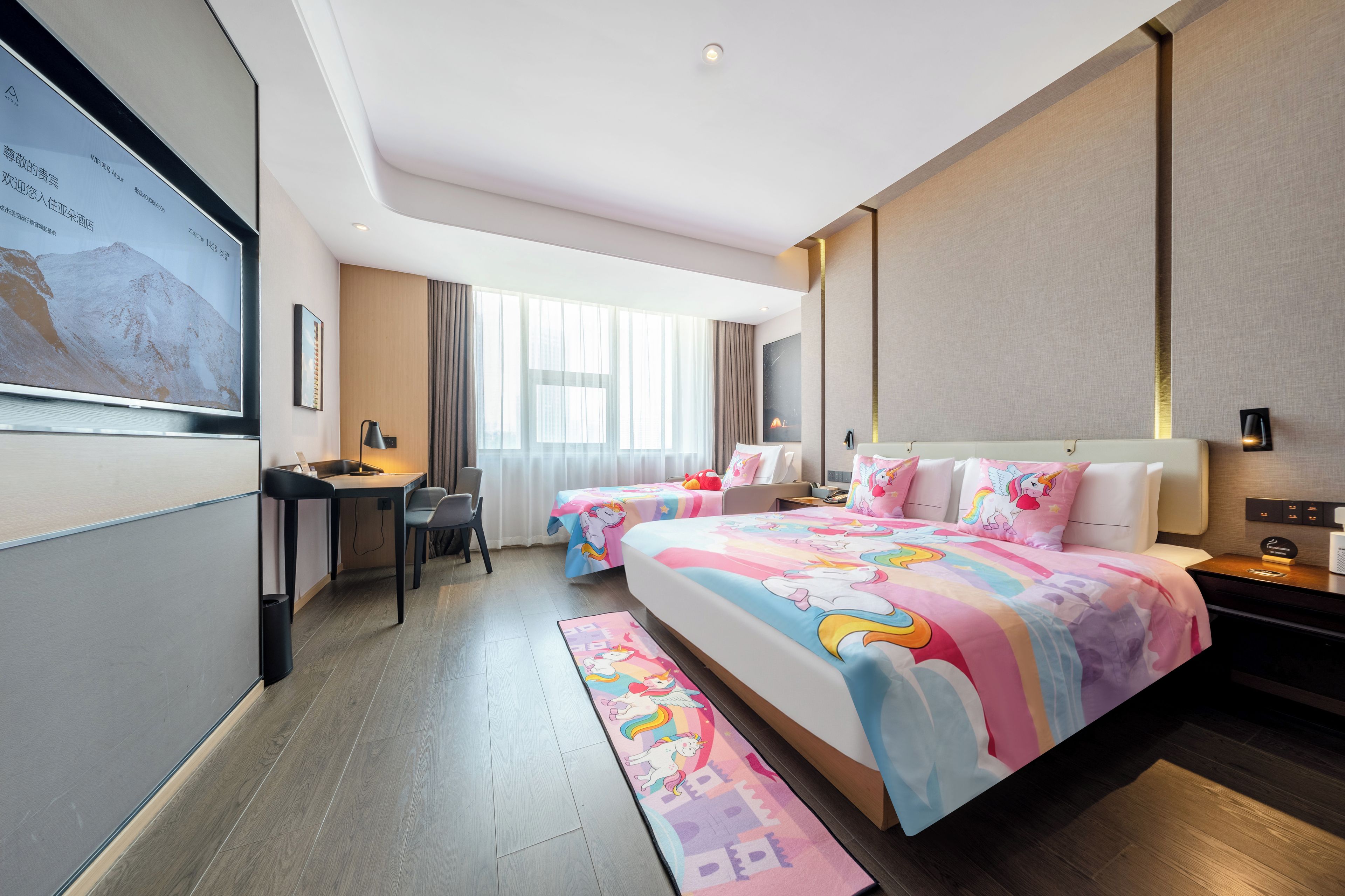 Una habitación de hotel con una cama grande, un escritorio y una silla. Hay una ventana con cortinas, un televisor montado en la pared y una cama con ropa de cama colorida.