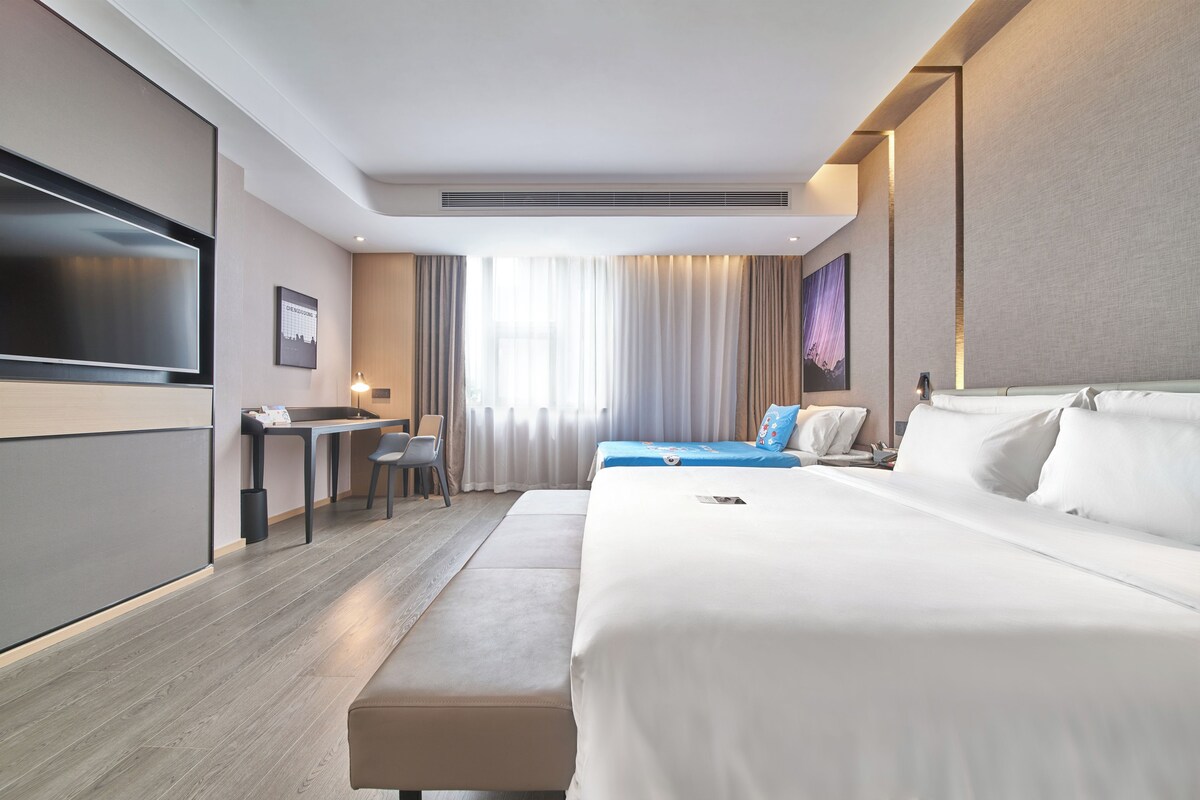 Una habitación de hotel con una cama grande, un escritorio, una silla, un televisor y una ventana con cortinas.