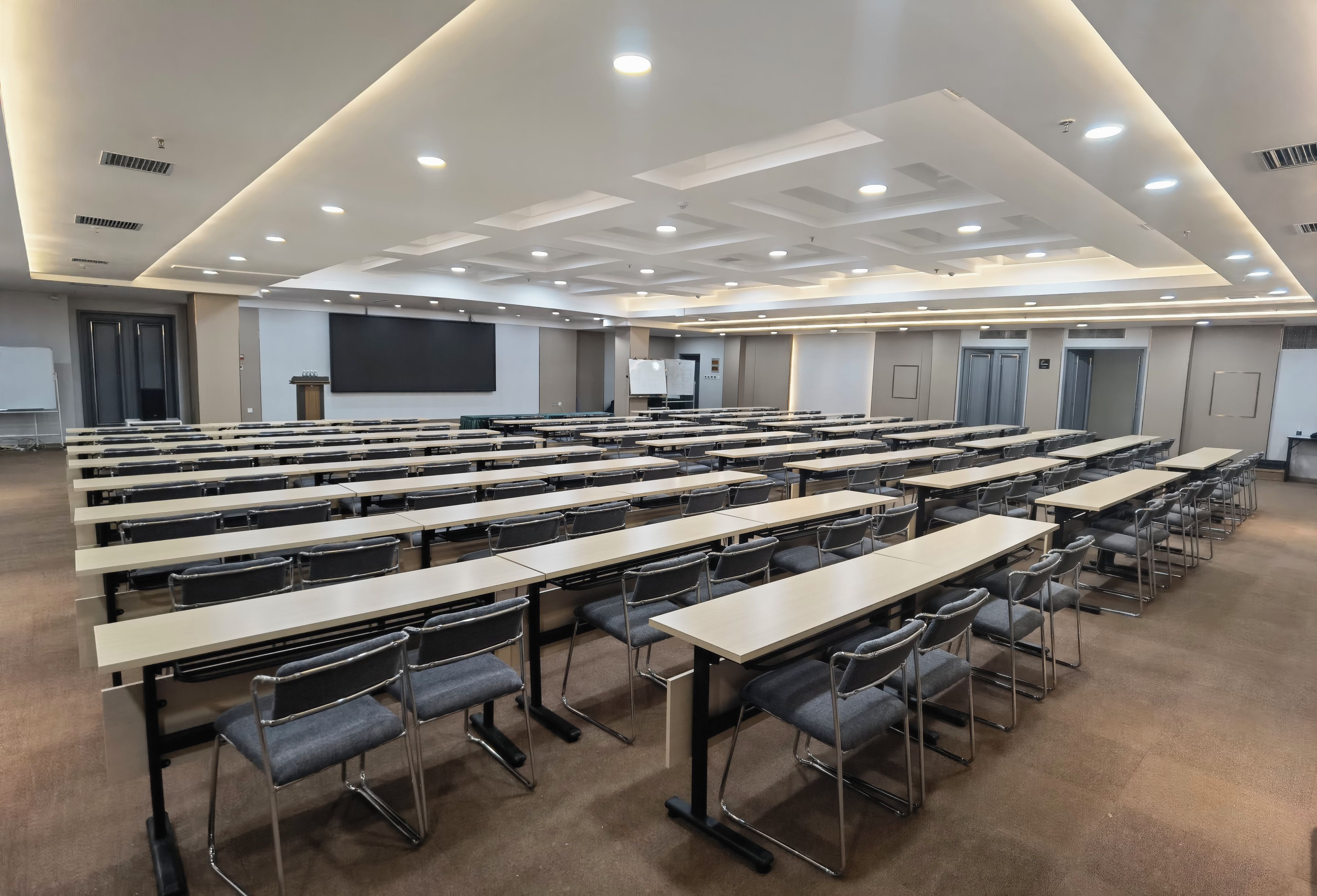 Une salle de conférence équipée de plusieurs tables et chaises, d’un grand écran et d’un pupitre.