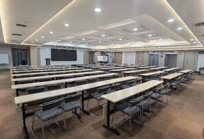 Una sala de conferencias con varias mesas y sillas, una pantalla grande y un atril.