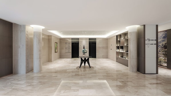 A modern hotel lobby with a marble floor, a central round table, and a reception desk.