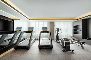 Et moderne fitnessrum med løbebånd, crosstrainer og bænk.