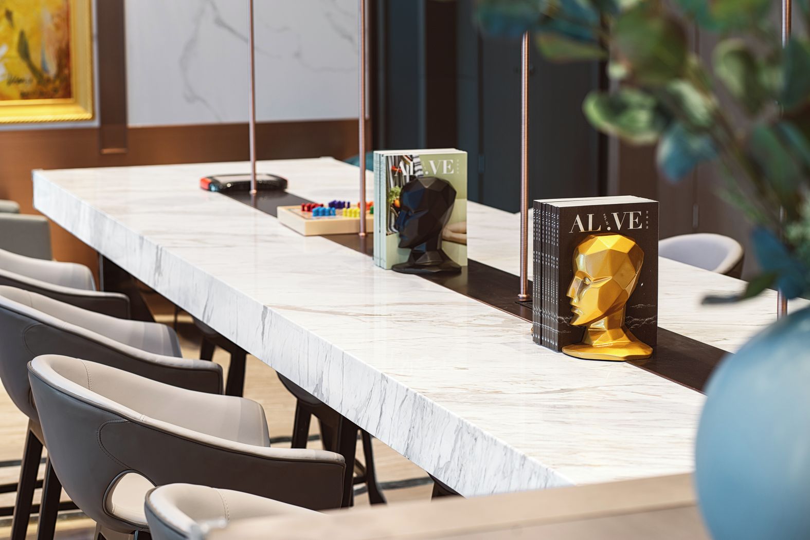 Una larga mesa con cubierta de mármol, un libro titulado 'ALIVE' y un busto dorado.