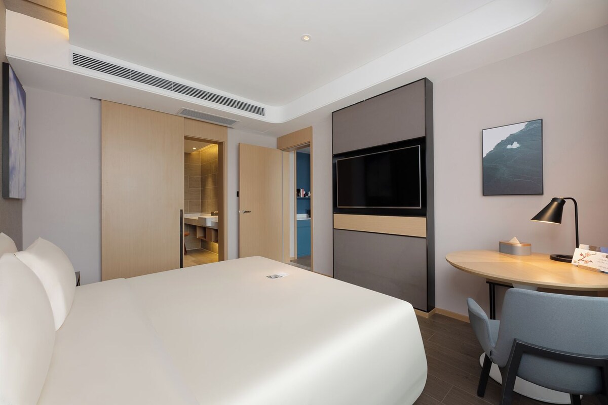 Una habitación de hotel moderna con una cama grande, un escritorio con una silla, un televisor de pantalla plana y un cuadro en la pared.