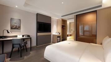 A modern hotel room with a bed, desk, chair, and a television.