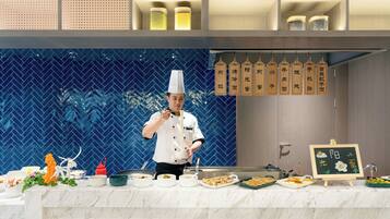 A chef preparing food in a modern kitchen with a blue herringbone tile backsplash, a marble countertop, and various dishes and ingredients.
