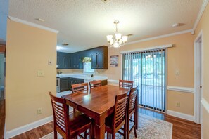 A dining area with a wooden table and chairs, a chandelier, and a view through a sliding glass door. - Large Wooded Yard, 7 Mi to Truliant Amphitheater (Charlotte)
