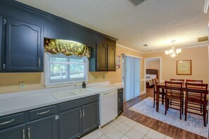 A kitchen with dark cabinets, a window with blinds, a sink, and a dining area with a table and chairs. - Large Wooded Yard, 7 Mi to Truliant Amphitheater (Charlotte)