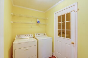 A laundry room with two white front-loading washers and dryers, a white door with a window, and a shelf with a detergent bottle. - Large Wooded Yard, 7 Mi to Truliant Amphitheater (Charlotte)