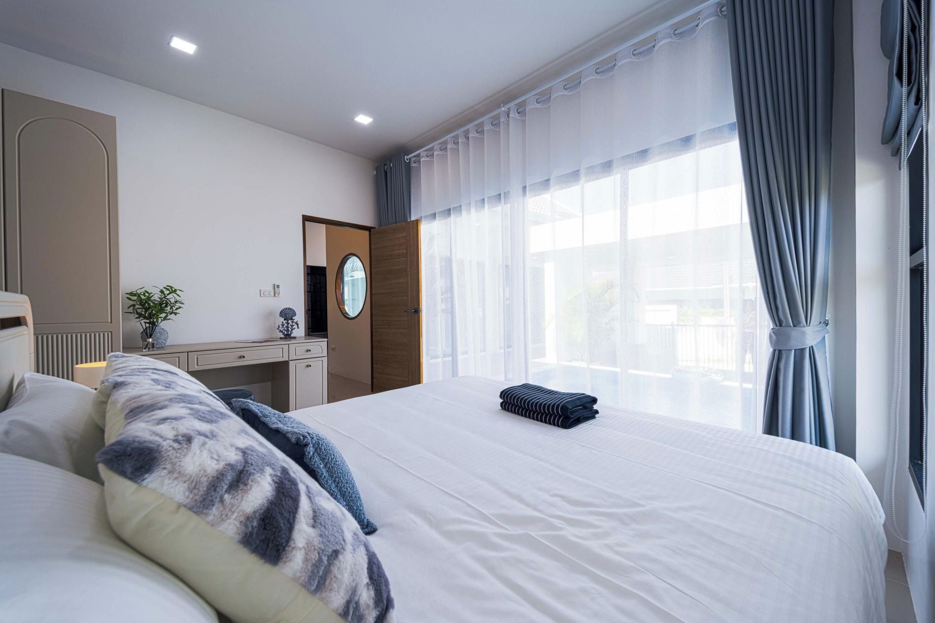 Quarto de hotel com uma cama grande, escrivaninha, espelho e janela com cortinas.