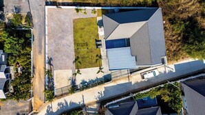 Luchtbeeld van een woonhuis met een groot zwembad, een tennisbaan en een oprit.