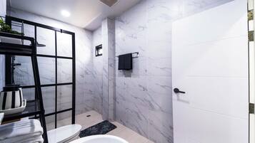 Un baño moderno con bañera, inodoro y zona de ducha, con paredes de mármol y un perchero negro.