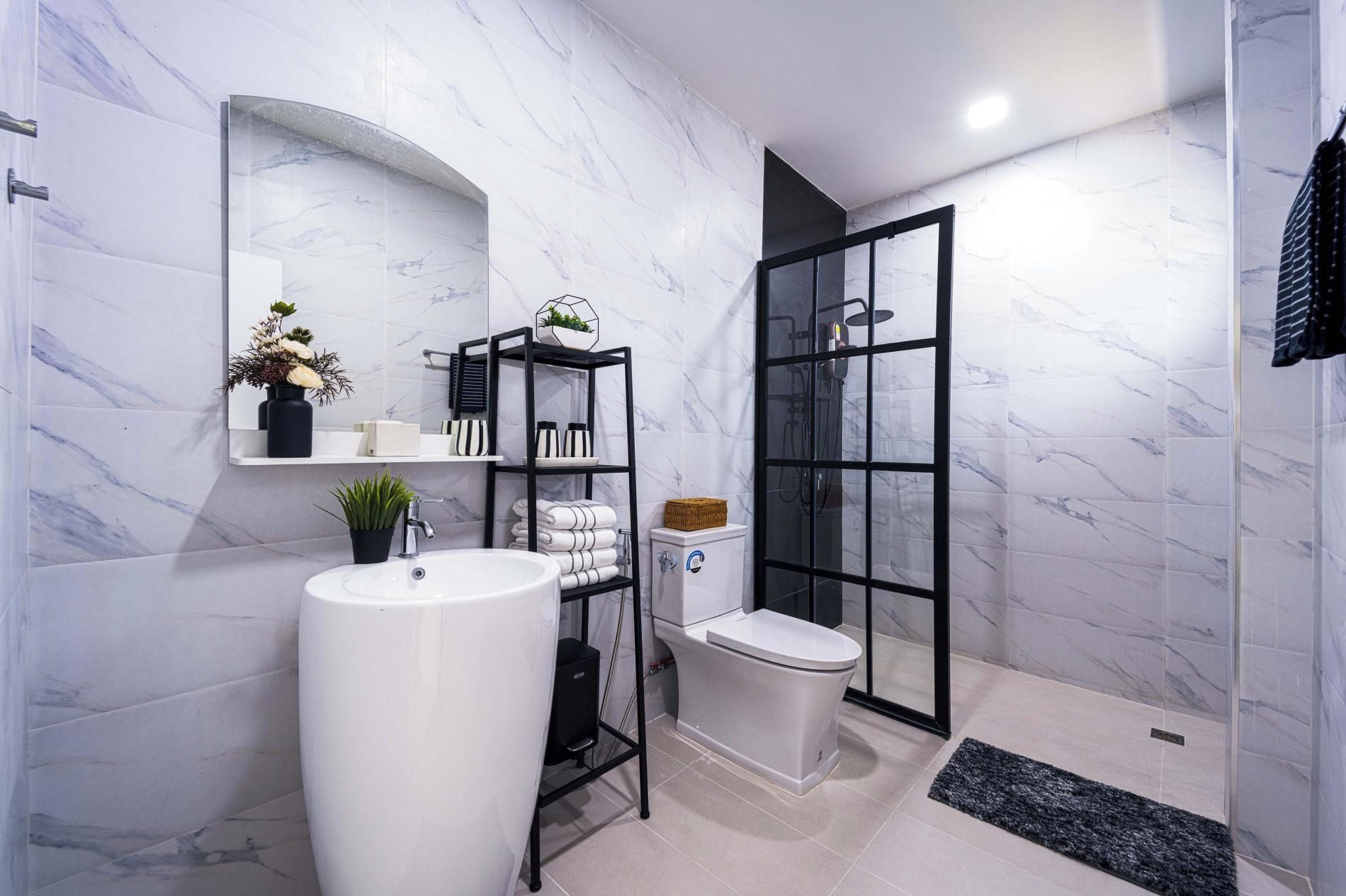 A modern bathroom with a white marble wall, a large sink, a toilet, and a glass shower enclosure.