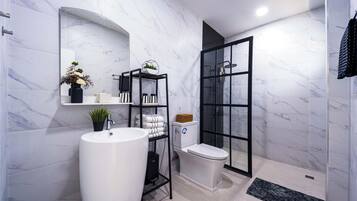 A modern bathroom with a white marble wall, a large sink, a toilet, and a glass shower enclosure.