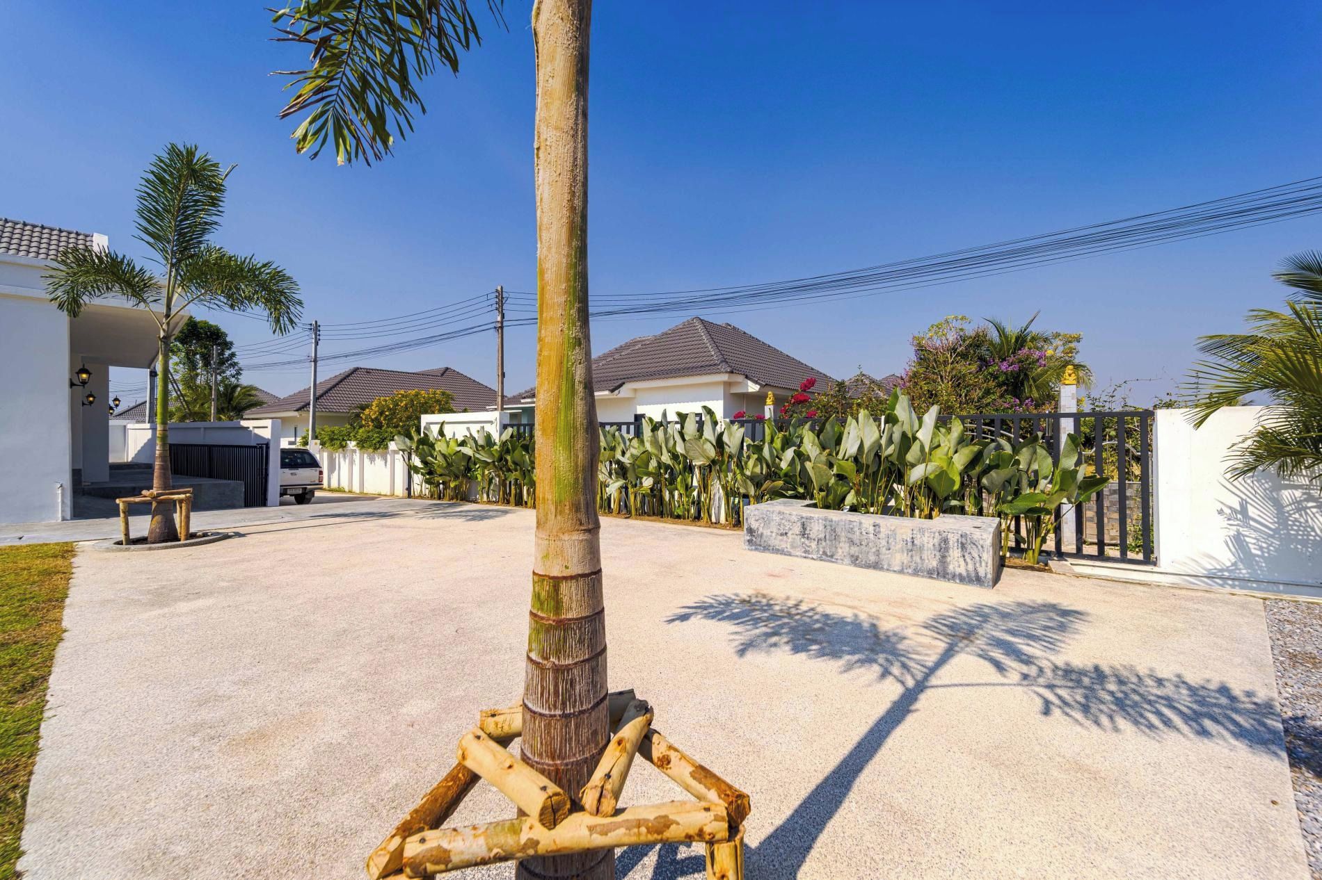 Zona residencial con una palmera, un banco de hormigón y una entrada con portón.