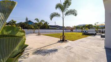 Un patio de concreto con una palmera, césped y una zona de estar con sillones reclinables.