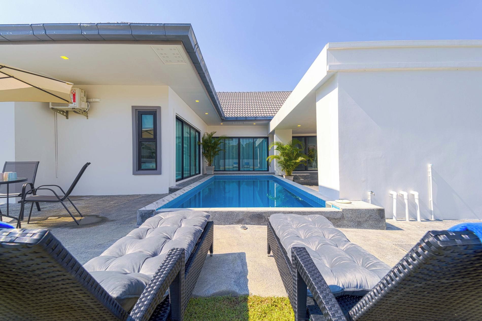 Un área de piscina moderna al aire libre con sillones de descanso, una zona de estar cubierta y una vista despejada de la piscina.