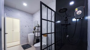 Een moderne badkamer met een douchecabine van glas, een toilet en een wit zuilenvormig wastafelmeubel.