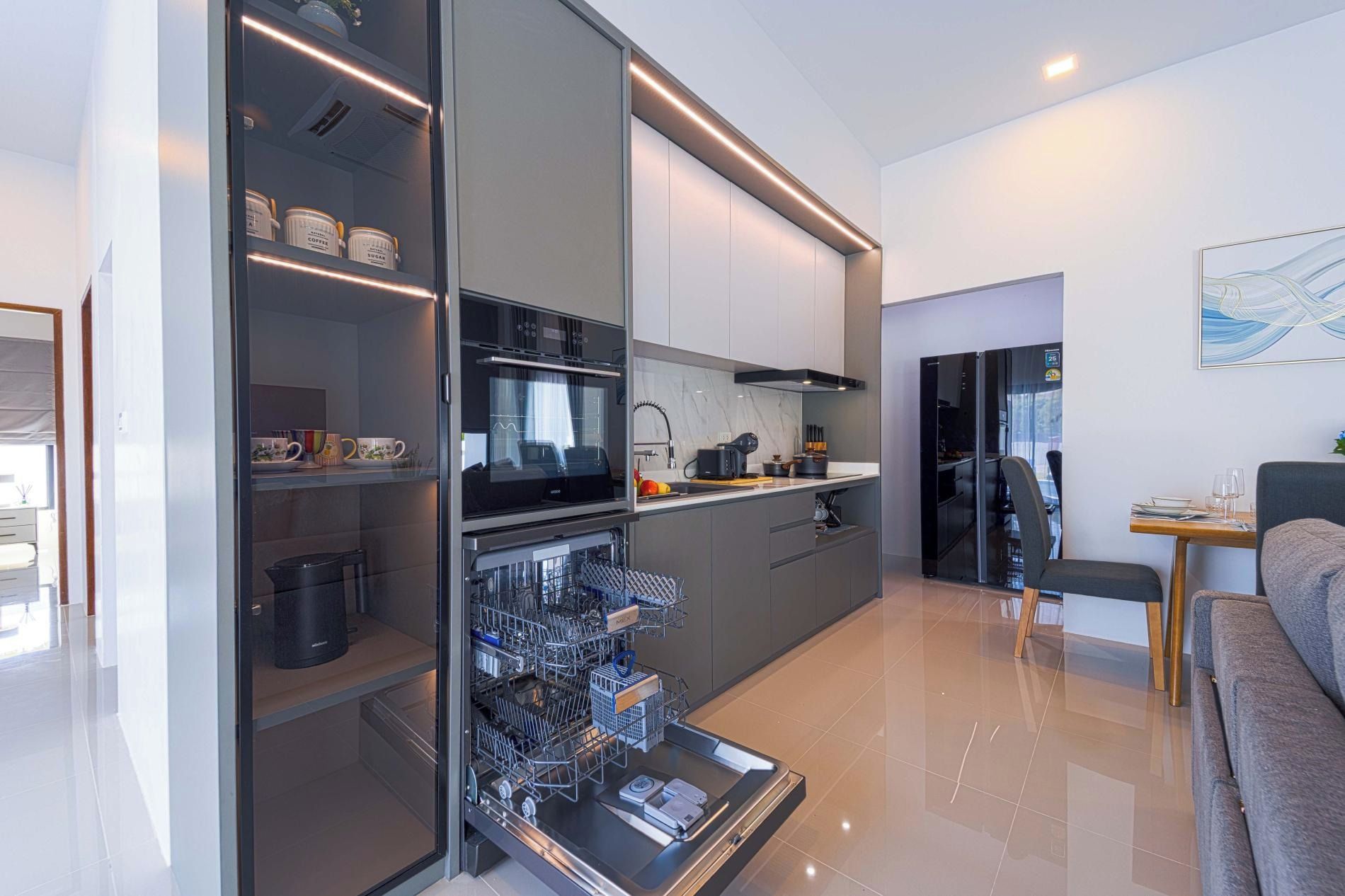 Uma cozinha moderna com máquina de lavar louça, frigorífico e zona de refeições com mesa e cadeiras.