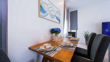 Un comedor con una mesa de madera dispuesta para cuatro, un jarrón con flores azules y un cuadro abstracto moderno en la pared.