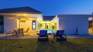Een modern huis met een zwembad, terrasmeubels en een goed verlicht terras.