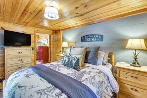 A cozy bedroom with a large bed, a television, wooden furniture, and a sign on the wall. - 'Wolf Ridge Lodge' w/ Hot Tub & Fire Pit! (Mena)