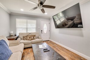 A living room with a ceiling fan, a sofa, a coffee table, and a TV mounted on the wall. - Walk to AT&T Stadium! Massage Chair & Cowboy Pool (Arlington)