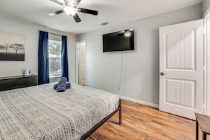 A bedroom with a bed, a ceiling fan, a flat-screen TV mounted on the wall, and a door. - Walk to AT&T Stadium! Massage Chair & Cowboy Pool (Arlington)