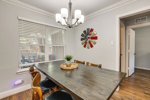 A dining room with a wooden table, chairs, a chandelier, a window with blinds, and a wall decoration. - Walk to AT&T Stadium! Massage Chair & Cowboy Pool (Arlington)