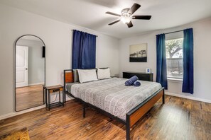 A bedroom with a bed, a bedside table, a mirror, a ceiling fan, and a window with curtains. - Walk to AT&T Stadium! Massage Chair & Cowboy Pool (Arlington)