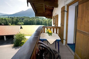 Varanda com mesa e cadeiras, vista para um campo gramado e montanhas.