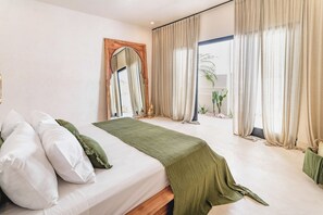 A bedroom with a large bed, a mirror, and a view of a cactus garden through the window.