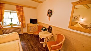 Um quarto acolhedor com piso de madeira, uma cama, uma mesa com cadeiras, uma televisão e um espelho.