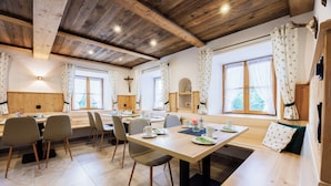 Uma sala de jantar com mesas e cadeiras de madeira, um banco e uma cruz na parede.
